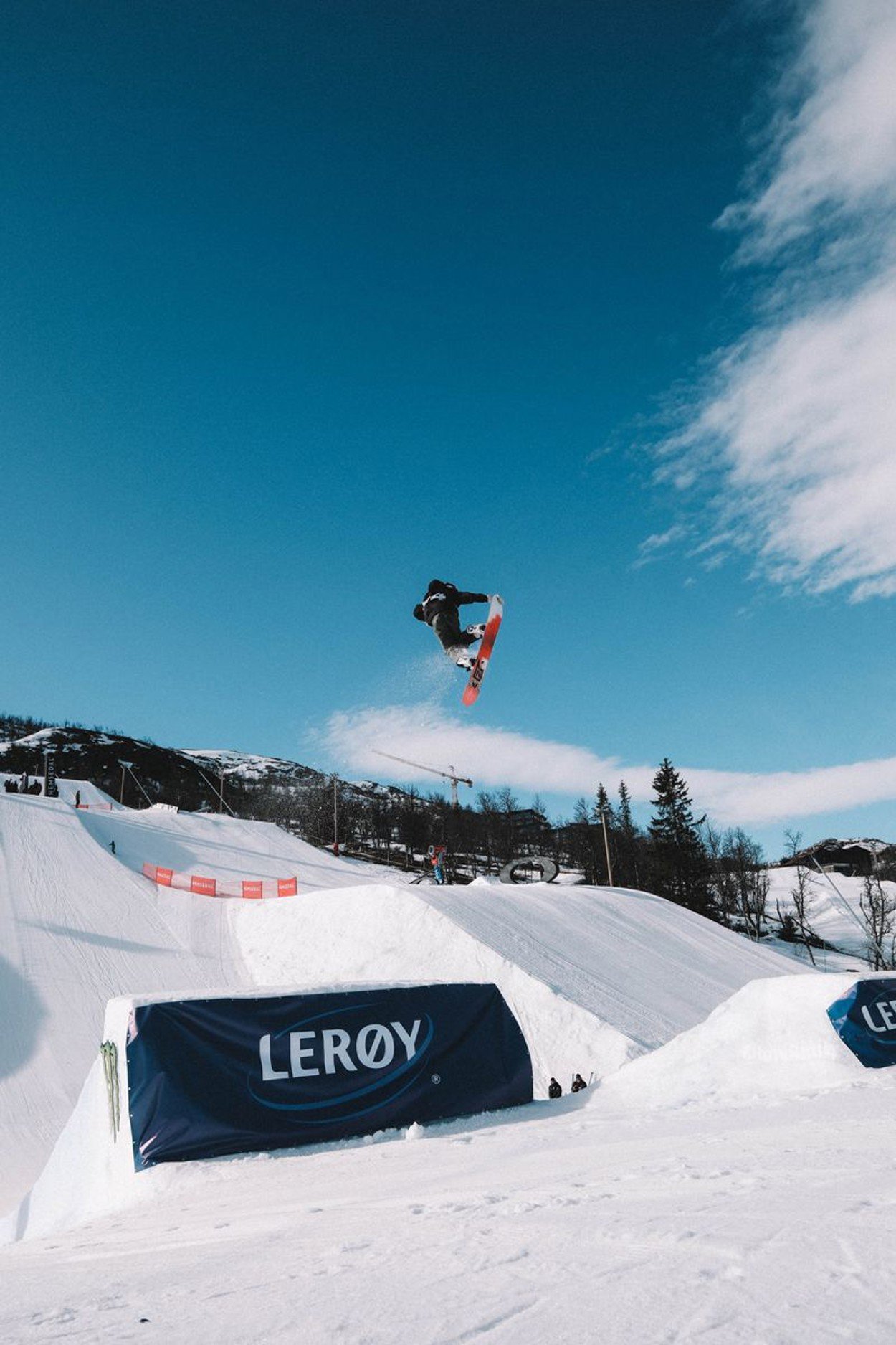 Picture taken from beneath; you can see a man jumping on a snowboard with blue skies with clouds.